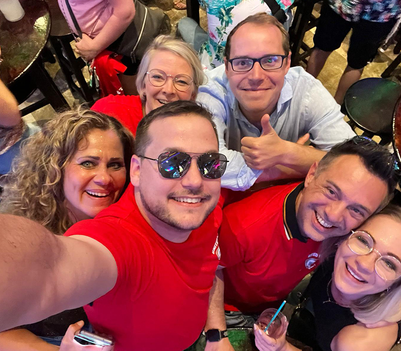 drei Mitarbeiter und drei Mitarbeiterinnen der Kanzlei machen zusammen ein Selfie beim Betriebsausflug. Sie sind im Bierkoenig auf Mallorca, tragen alle bis auf einen rote T-Shirts und sehen sehr gut gelaunt aus.
