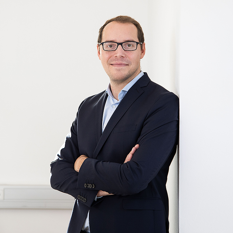 Steuerberater Robert Kopiec lehnt in blauem Jacket an weißer Wand