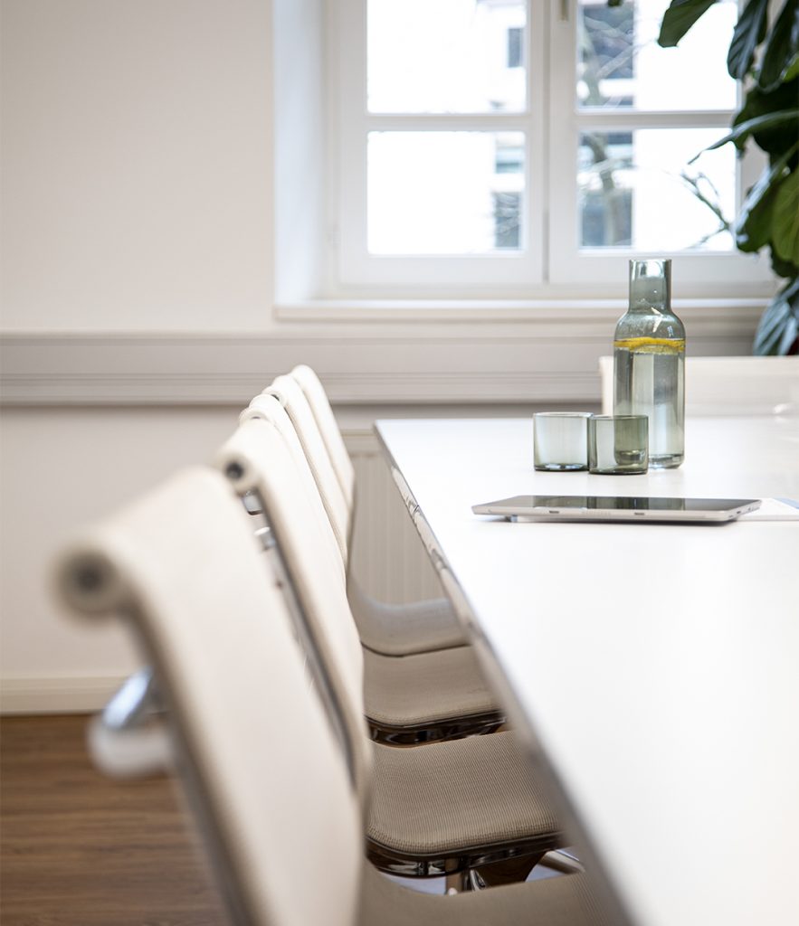 Tablet und Wasserkaraffe stehen auf einem weissen Vitra Tisch mit weissen Vitra Stühlen